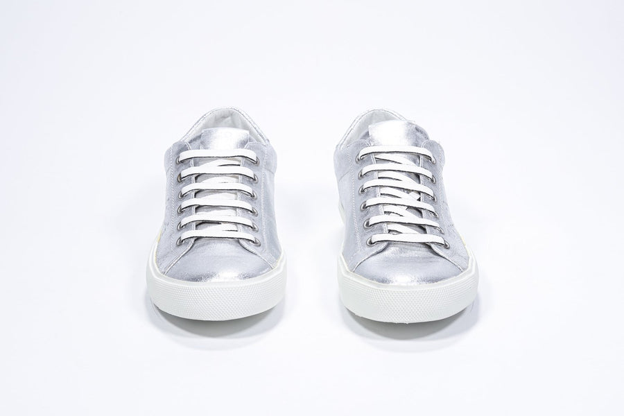 Vorderansicht eines silbernen Low-Top-Sneakers mit perforiertem Kronenlogo auf dem Obermaterial. Obermaterial aus Metallic-Leder und weiße Gummisohle.