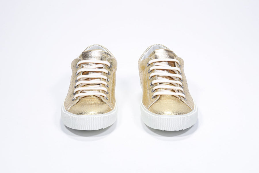Vorderansicht eines goldenen Low-Top-Sneakers mit perforiertem Kronenlogo auf dem Obermaterial. Obermaterial aus Metallic-Leder und weiße Gummisohle.