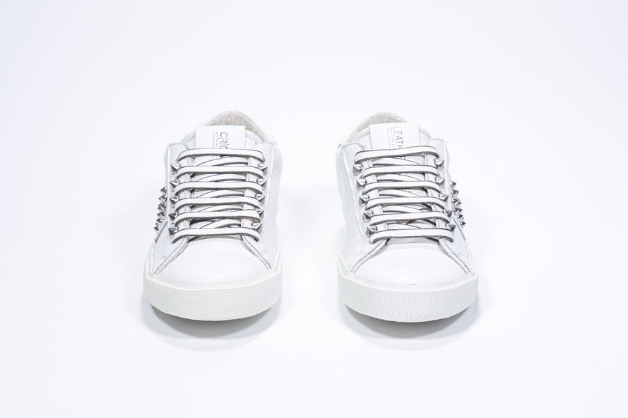 Vorderansicht eines weißen Low-Top-Sneakers. Obermaterial aus Vollleder mit Nieten und weißer Gummisohle.