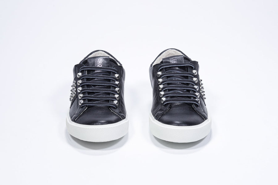Vorderansicht eines schwarzen Low-Top-Sneakers. Obermaterial aus Vollleder mit Nieten und weißer Gummisohle.