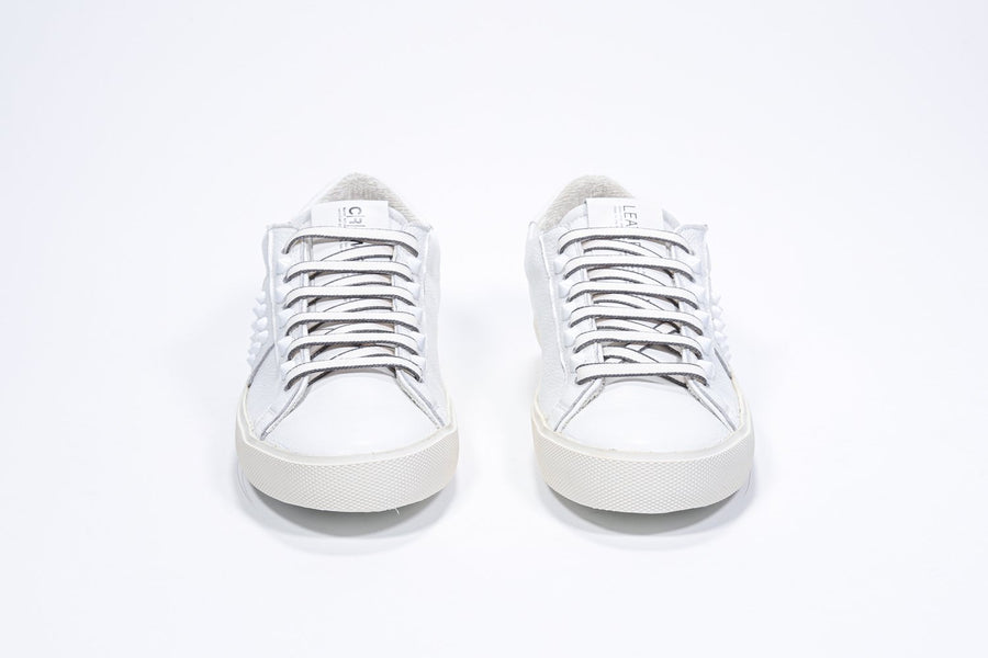 Vorderansicht eines weißen Low-Top-Sneakers. Obermaterial aus Vollleder mit Nieten und Vintage-Gummisohle.
