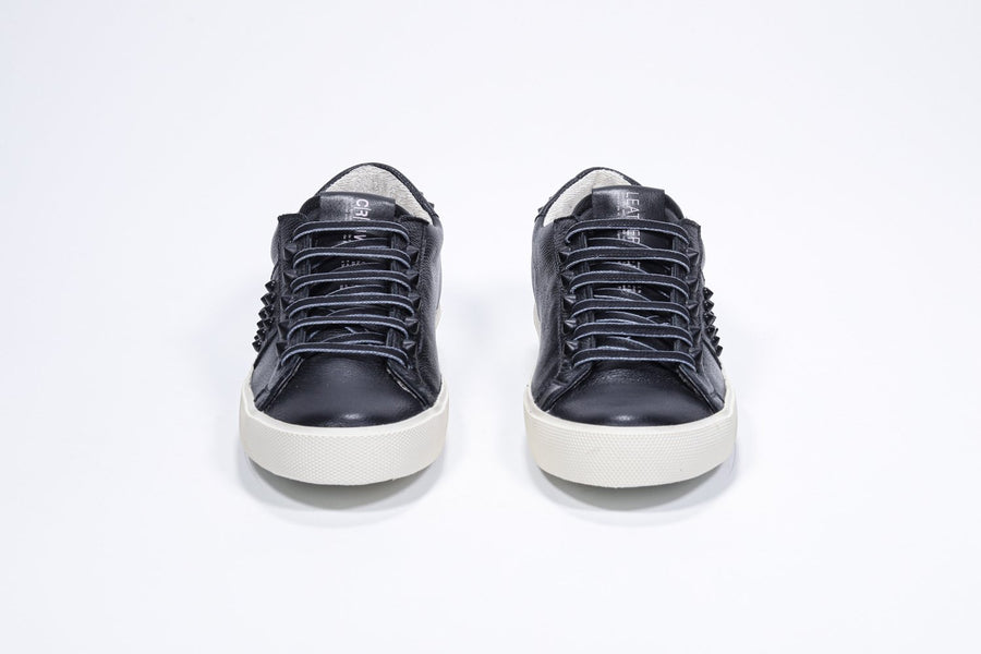 Vorderansicht eines schwarzen Low-Top-Sneakers. Obermaterial aus Vollleder mit Nieten und Vintage-Gummisohle.