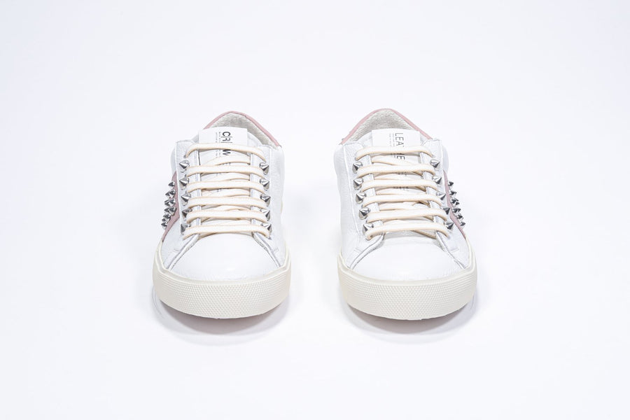Vorderansicht eines weißen und blassrosa Sneakers mit niedrigem Schaft. Obermaterial aus Vollleder mit Nieten und Vintage-Gummisohle.