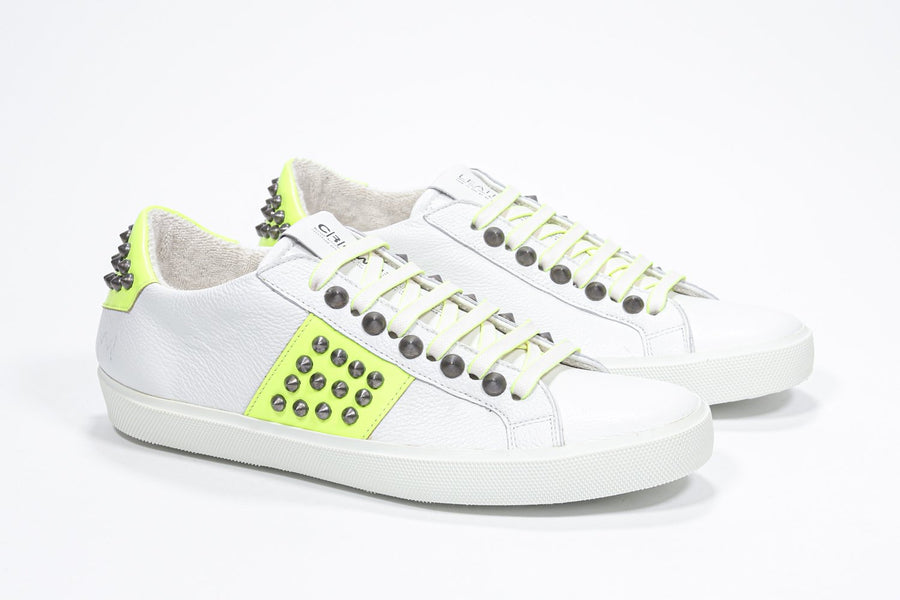 Dreiviertelansicht der Vorderseite eines weißen und neongelben Low-Top-Sneakers. Obermaterial aus Vollleder mit Nieten und weißer Gummisohle.