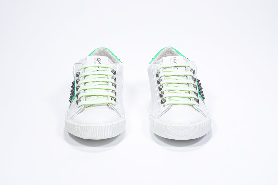 Vorderansicht eines weißen und neongrünen Low-Top-Sneakers. Obermaterial aus Vollleder mit Nieten und weißer Gummisohle.