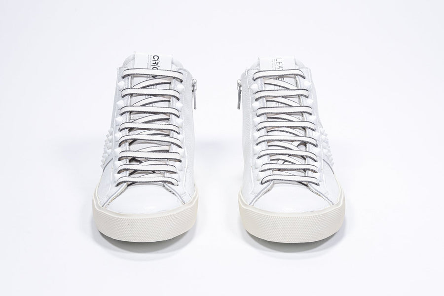 Vorderansicht eines weißen Mid-Top-Sneakers. Obermaterial aus Vollleder mit Nieten, einem internen Reißverschluss und einer Vintage-Gummisohle.