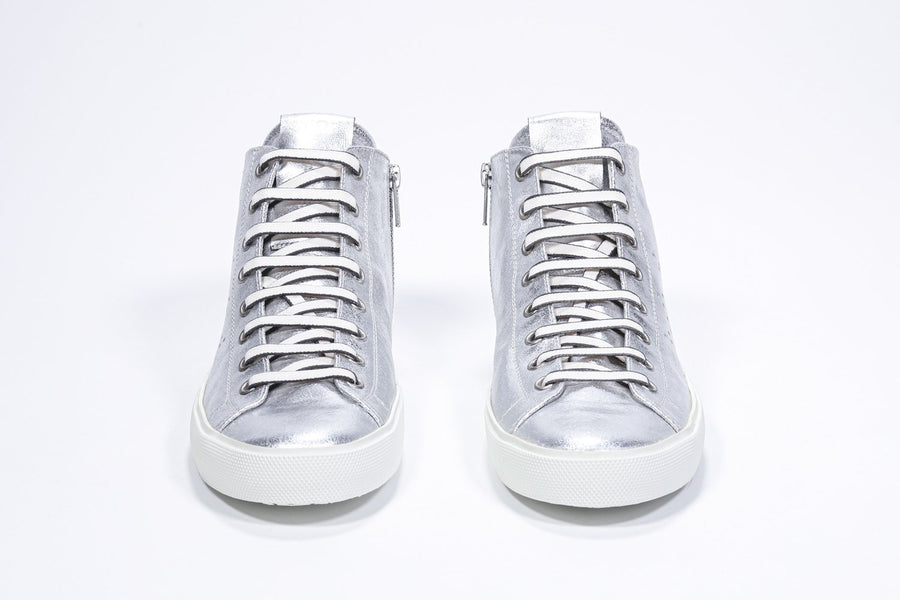 Vue de face d'une chaussure de sport argentée à tige en cuir avec logo perforé, fermeture éclair intérieure et semelle blanche.