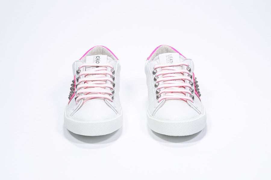 Vista frontale della sneaker low top bianca e rosa neon. Tomaia in pelle con borchie e suola in gomma bianca.