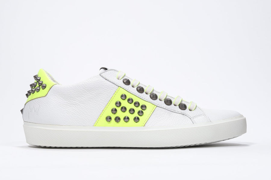 Profilo laterale di una sneaker low top bianca e giallo neon. Tomaia in pelle con borchie e suola in gomma bianca.